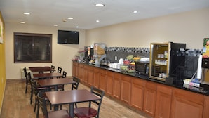 A restaurant with wooden tables and chairs, a kitchen counter with appliances, and a tiled backsplash. - Super 8 by Wyndham Webster City IA (Webster City)