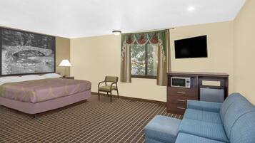 Habitación de hotel con cama, sofá azul, escritorio con microondas, silla, televisor y ventana con cortinas.