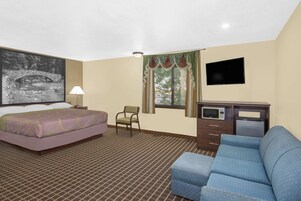 Habitación de hotel con cama, sofá azul, escritorio con microondas, silla, televisor y ventana con cortinas.