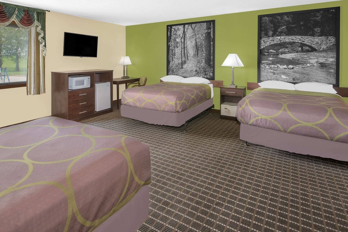 A hotel room with two beds, a desk with a computer, a TV, and artwork on the walls.
