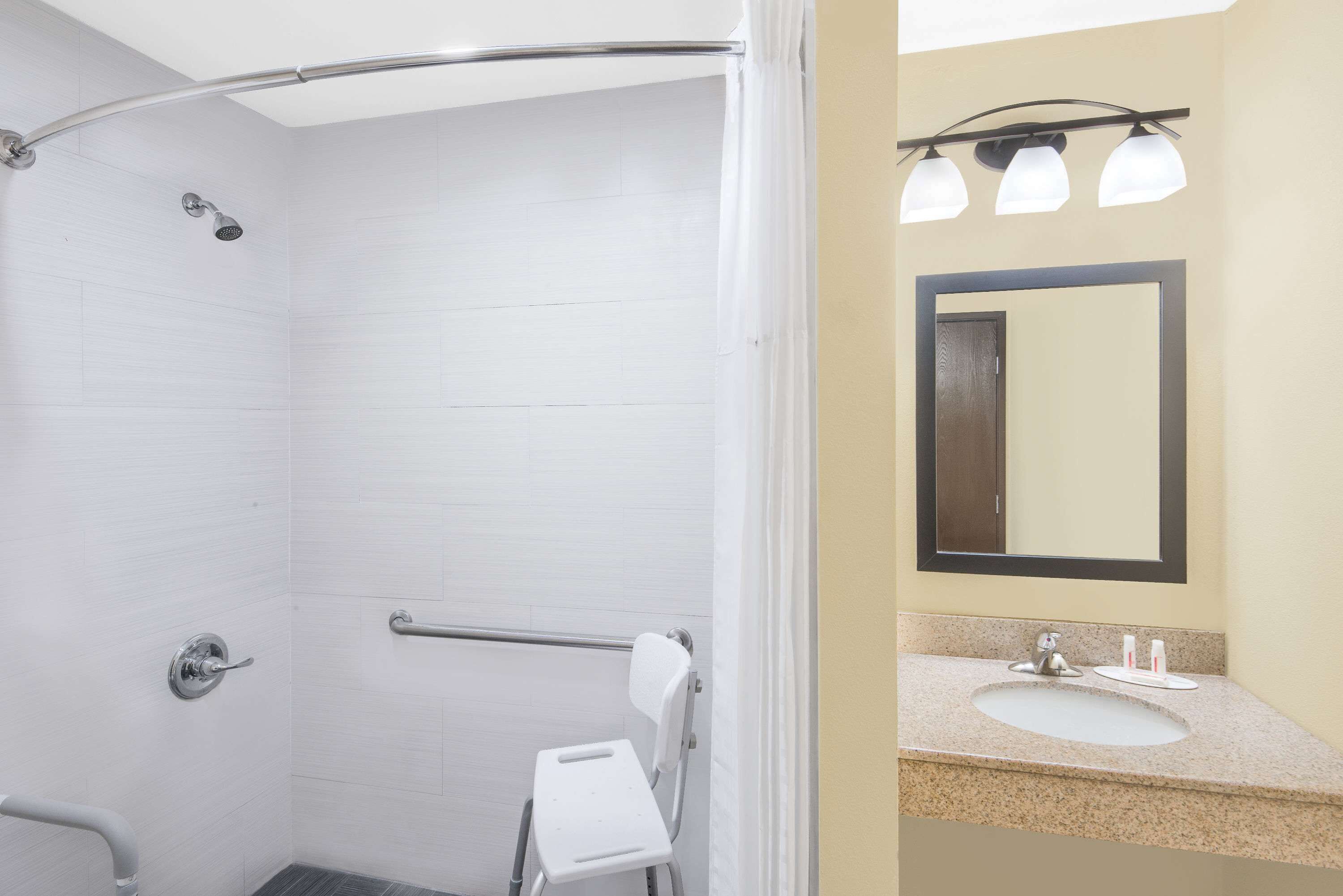 A bathroom with a shower, a handrail, a grab bar, a sink, and a mirror.