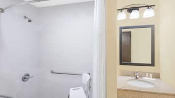 A bathroom with a shower, a handrail, a grab bar, a sink, and a mirror.