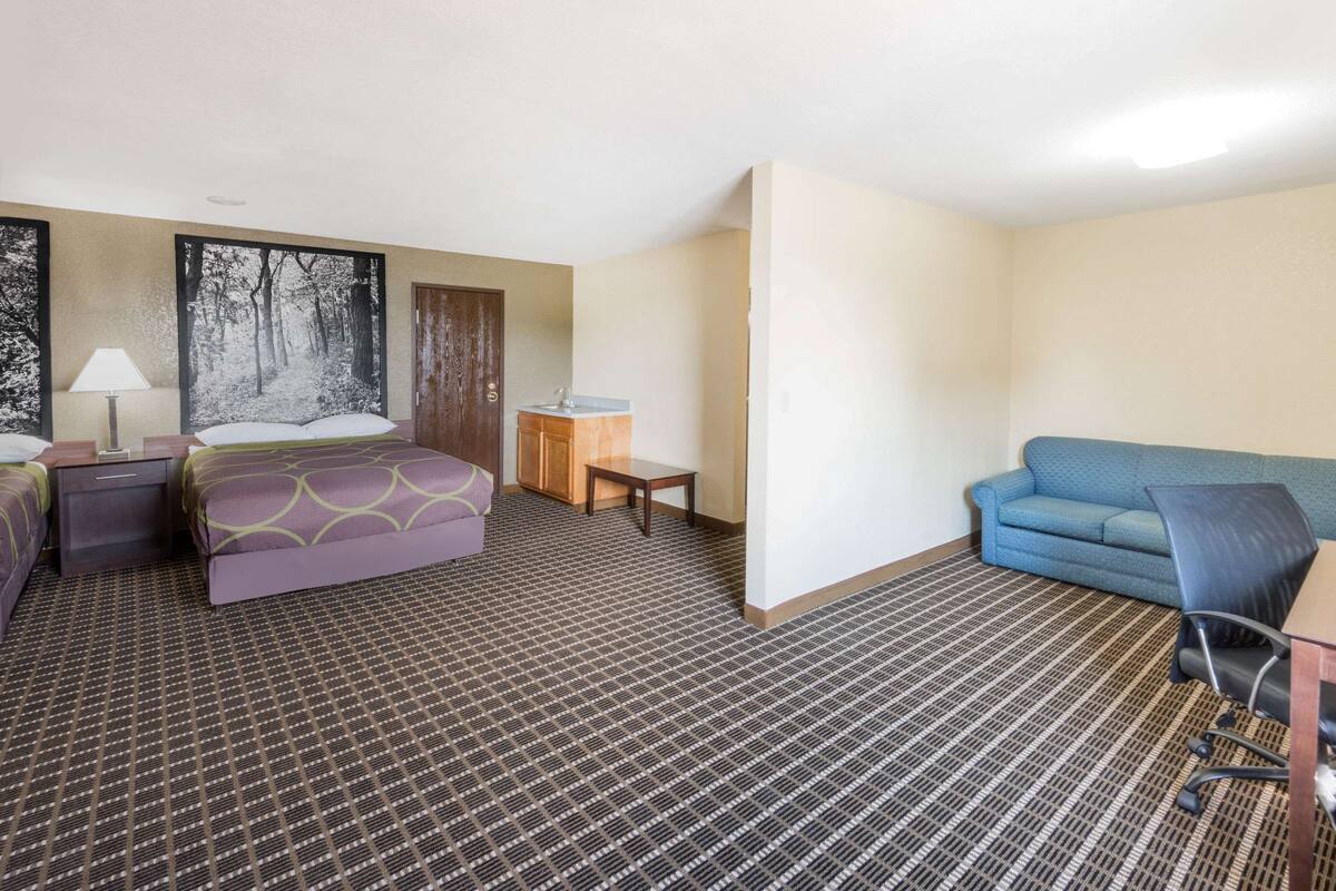 A hotel room with a bed, a desk, a chair, a sofa, and a painting on the wall.
