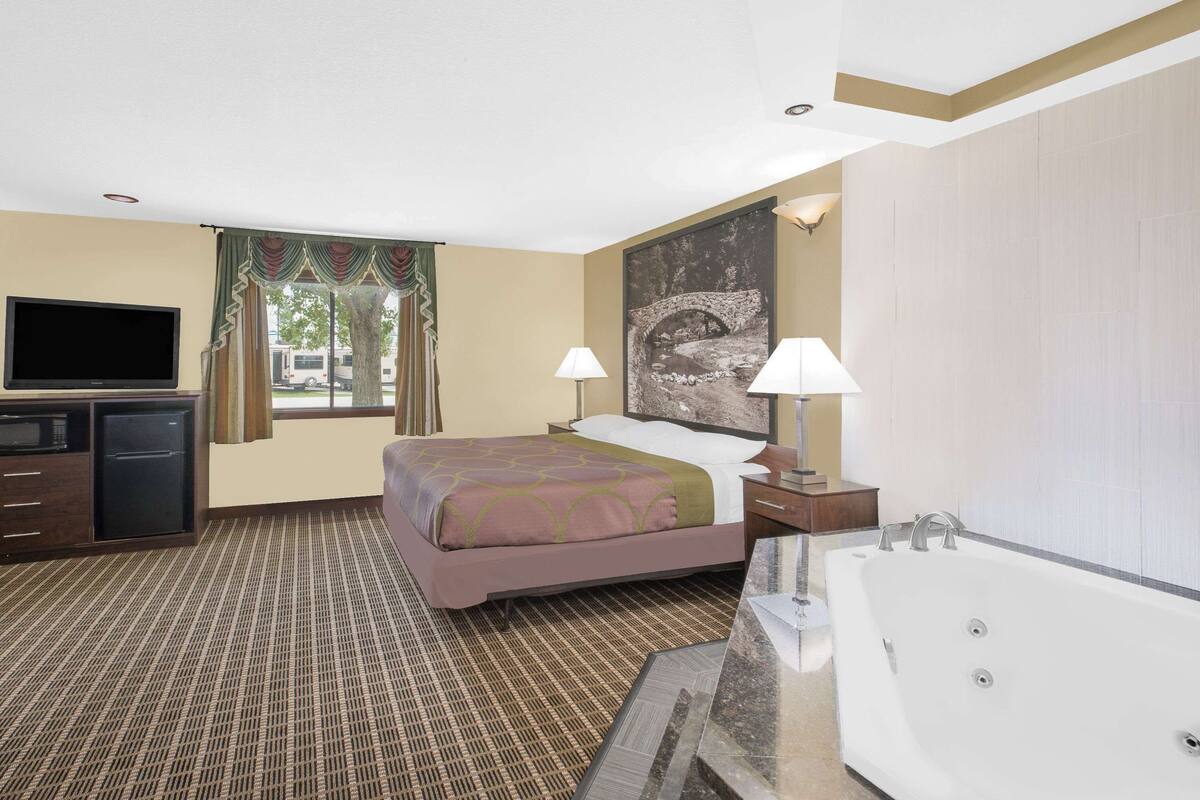 A hotel room with a bed, a TV, a desk, a lamp, and a bathtub.