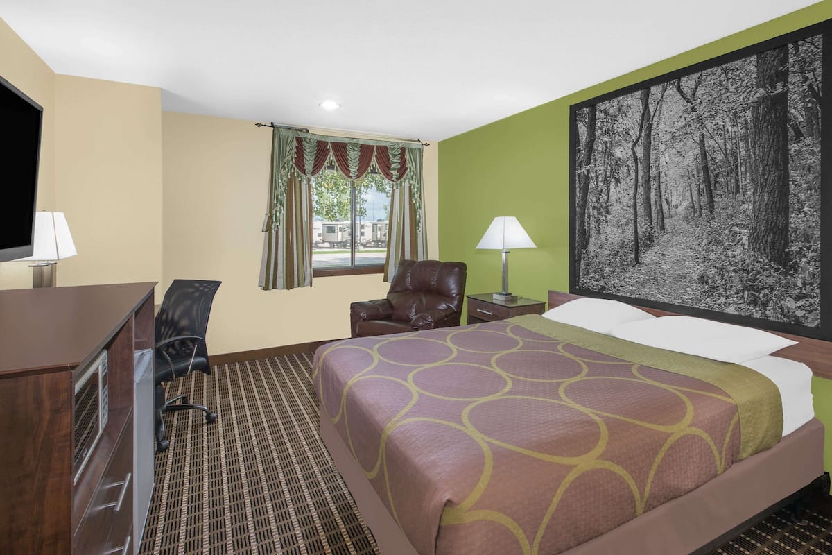 A hotel room with a bed, a desk, a chair, a TV, and a window with curtains.