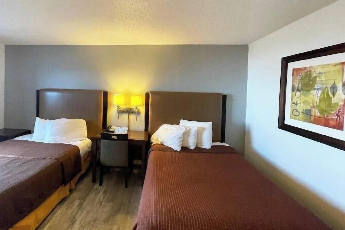 A hotel room with two single beds, a nightstand with a lamp, and a framed picture on the wall.