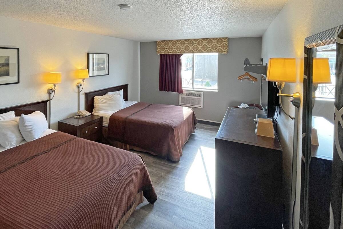 A hotel room with two beds, bedside lamps, a desk with a mirror, and a window with curtains.