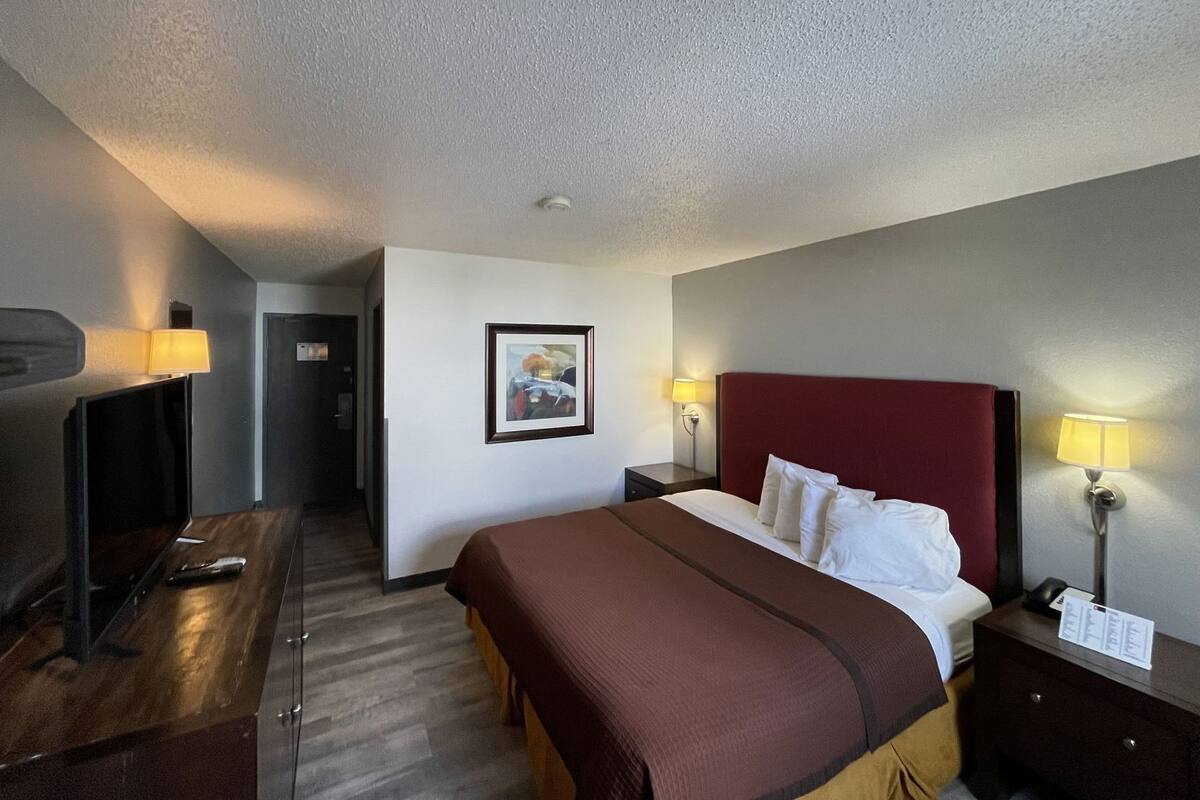 A hotel room with a bed, bedside tables, a desk, and a framed picture on the wall.