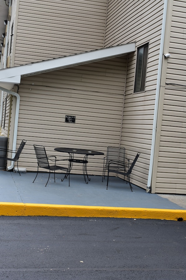 En hjørnehævet terrasse med et bord og stole, et skilt der fremhæver et designelement, og en gul kantsten.