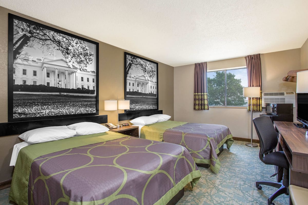 Une chambre d’hôtel avec deux lits, un bureau, une chaise, une télévision et de grandes photos encadrées de la Maison-Blanche.