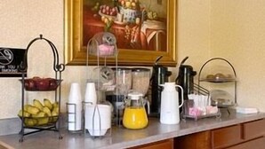 Una barra de desayuno con una cesta de frutas, cafetera y un cuadro de frutas en la pared.