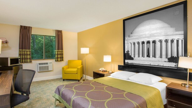 Habitación de hotel con una cama grande, un escritorio, una silla, una lámpara y un cuadro grande en la pared.