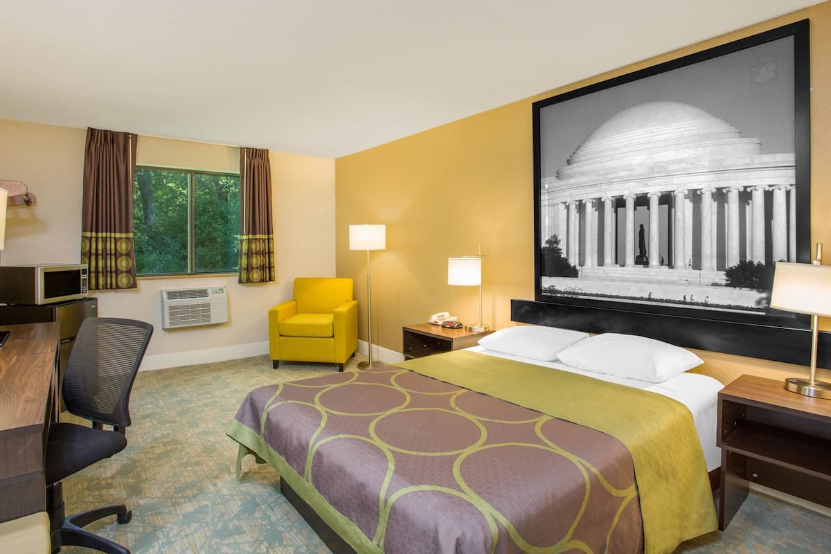 Une chambre d’hôtel avec un grand lit, un bureau, une chaise, une lampe et un grand tableau encadré au mur.