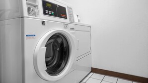 Lavadora de carga frontal en un cuarto de lavado con panel de control, una etiqueta de aviso y piso de baldosas.