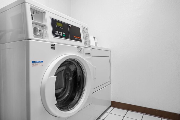 A front-loading washing machine in a laundry room with a control panel, a notice label, and a tiled floor.