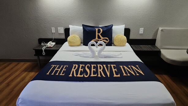 Ett hotellrum med en säng som har ett täcke med texten ”THE RESERVE INN”, två kuddar med svanmotiv och ett nattduksbord med en telefon.