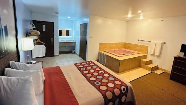 A hotel room with a bed, a large window, a bathroom with a bathtub, and a desk with a lamp. - Super 8 by Wyndham Imlay City (Imlay City)