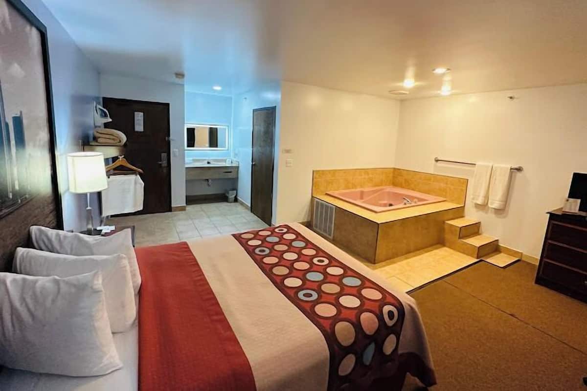 Ein Hotelzimmer mit Bett, großem Fenster, Badezimmer mit Badewanne und Schreibtisch mit Lampe.