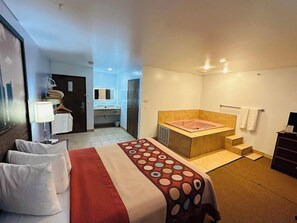 Ein Hotelzimmer mit Bett, großem Fenster, Badezimmer mit Badewanne und Schreibtisch mit Lampe.