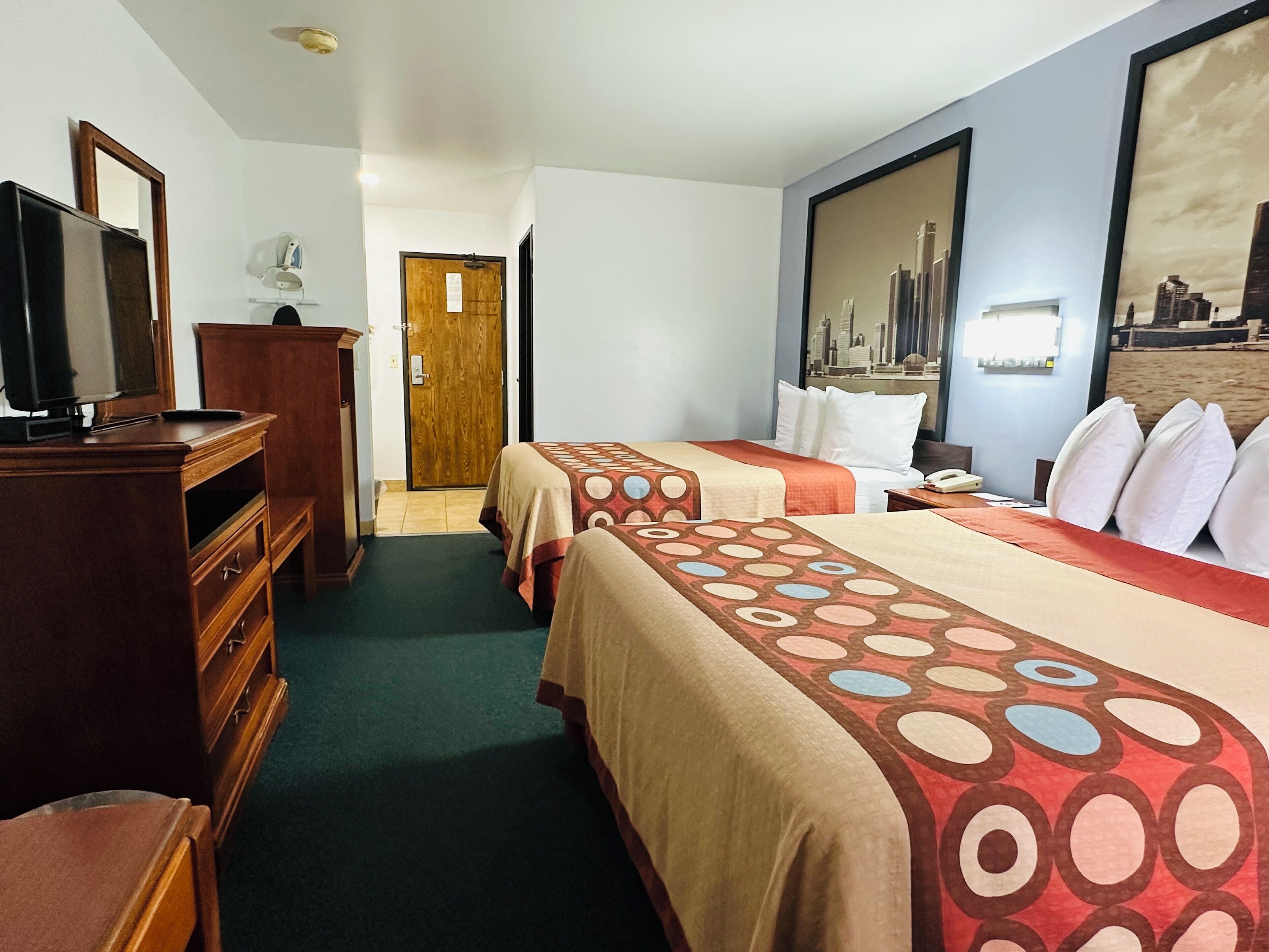 Une chambre d’hôtel avec deux lits, une télévision, une commode et une porte donnant sur une autre pièce.