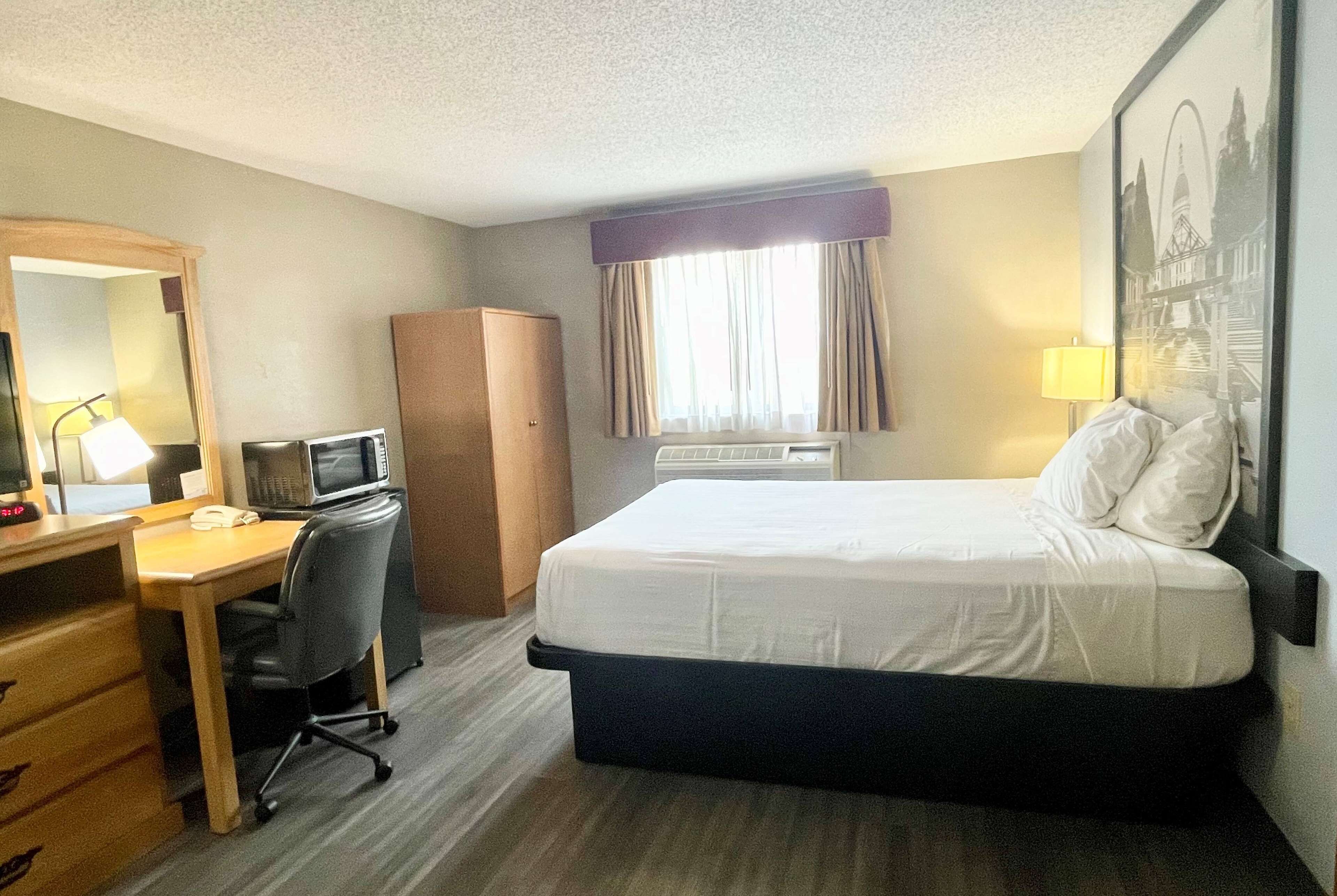 Ein Hotelzimmer mit Bett, Schreibtisch, Stuhl und einem großen Spiegel.