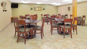 A dining area with multiple wooden tables and chairs, a television mounted on the wall, and a tiled floor. - Super 8 by Wyndham St. Clair MO (St. Clair)