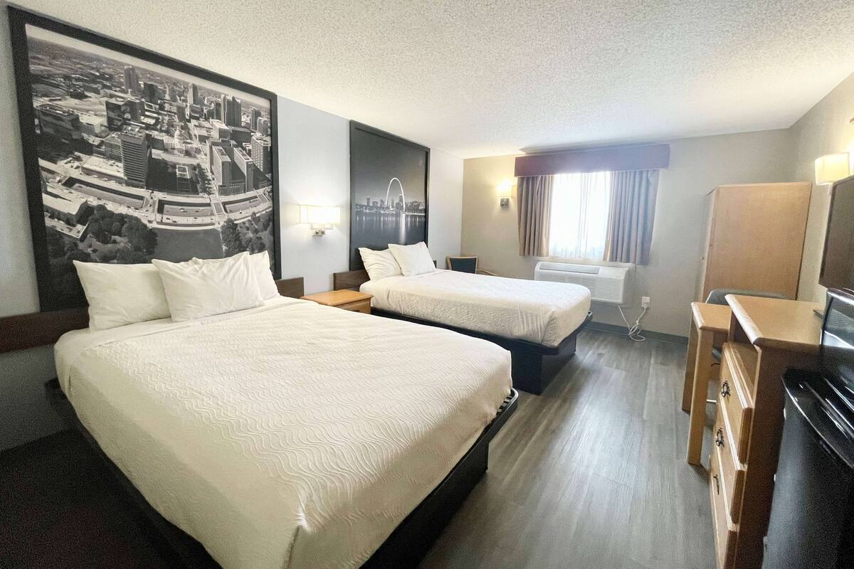 Een hotelkamer met twee bedden, een bureau, een stoel, een dressoir en een groot stadsgezichtschilderij aan de muur.