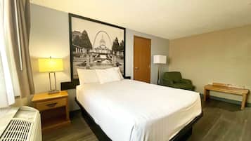 Habitación de hotel con cama, mesita de noche con lámpara, silla, banco y una obra de arte en la pared.