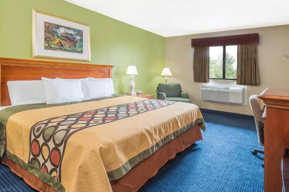 Een hotelkamer met een bed, een bureau, een stoel, een televisie, een raam met gordijnen en een schilderij aan de muur.