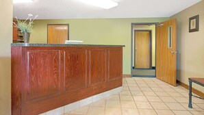 A reception area with a wooden reception desk, a vase with flowers, and a door leading to another room. - Super 8 by Wyndham St. Clair MO (St. Clair)