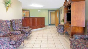 A spacious lobby with floral-patterned armchairs, a wooden reception desk, and a television on a wooden cabinet. - Super 8 by Wyndham St. Clair MO (St. Clair)