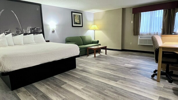 A hotel room with a bed, a green sofa, a small table, a desk, and a lamp. - Super 8 by Wyndham St. Clair MO (St. Clair)