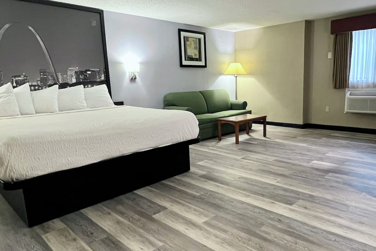 Een hotelkamer met een bed, een groene bank, een kleine tafel, een bureau en een lamp.