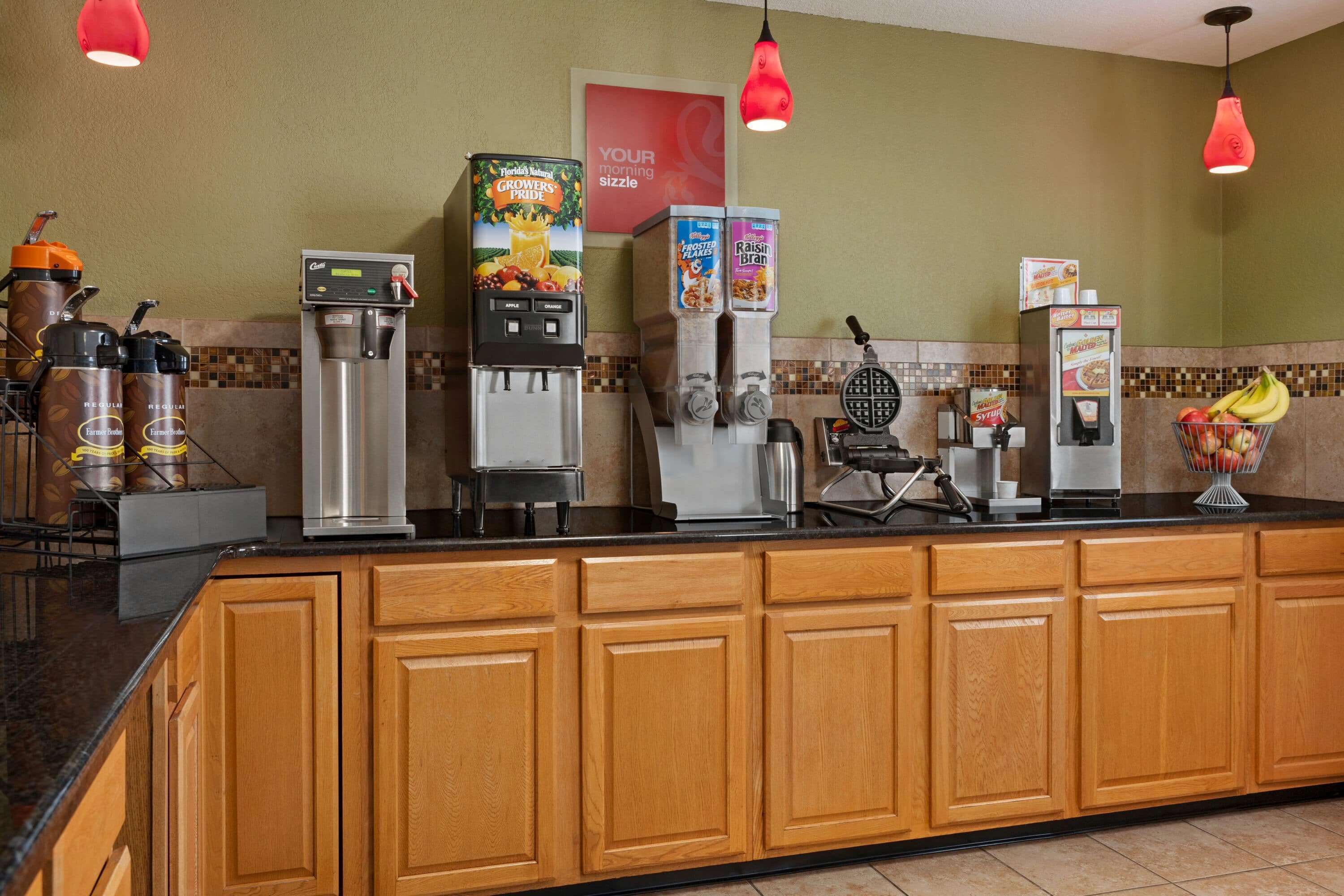 A self-service breakfast bar with coffee machines, a waffle maker, and refrigerated beverage dispensers.