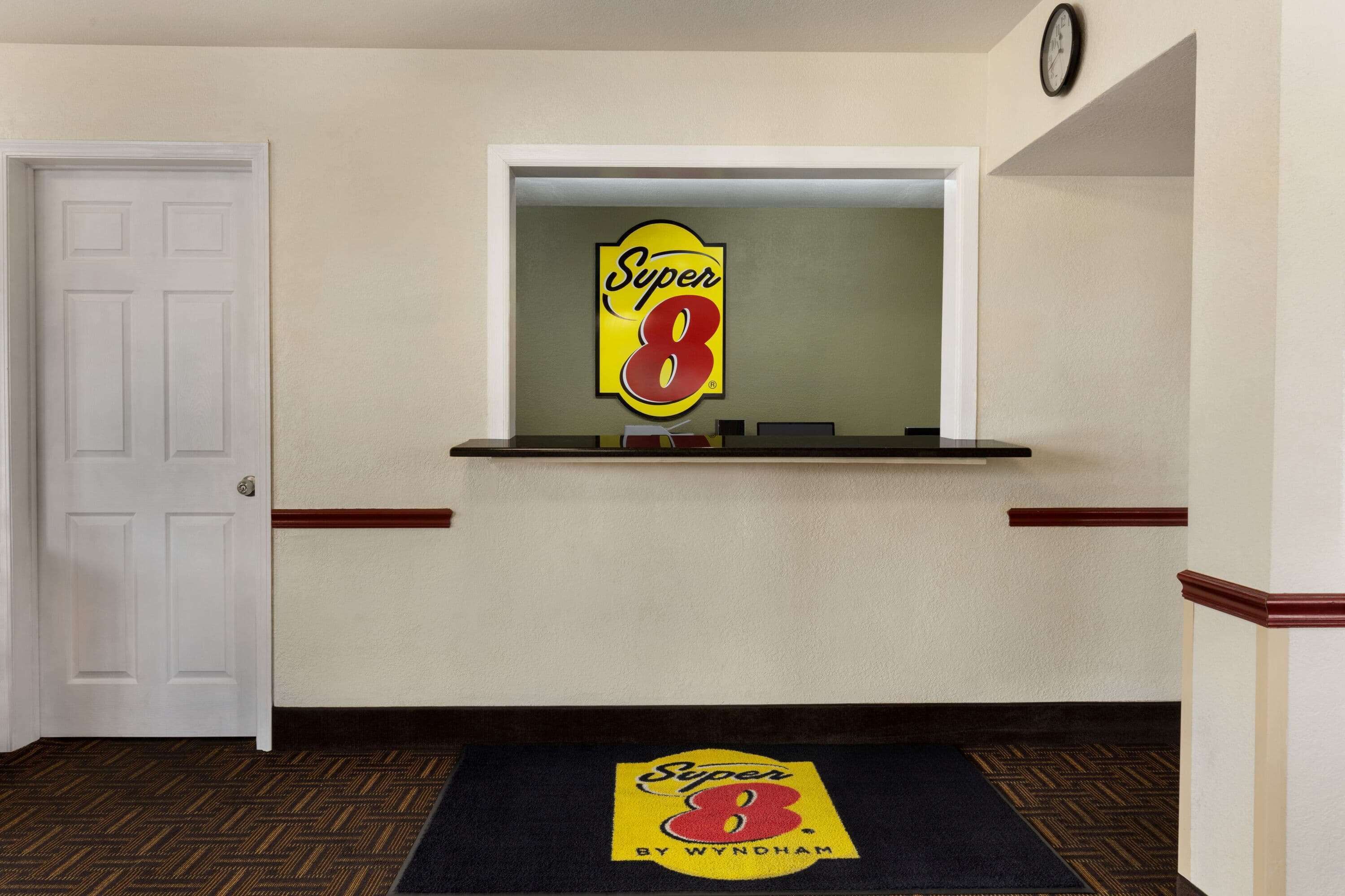 A hallway with a reception area featuring a 'Super 8' sign and a clock on the wall.