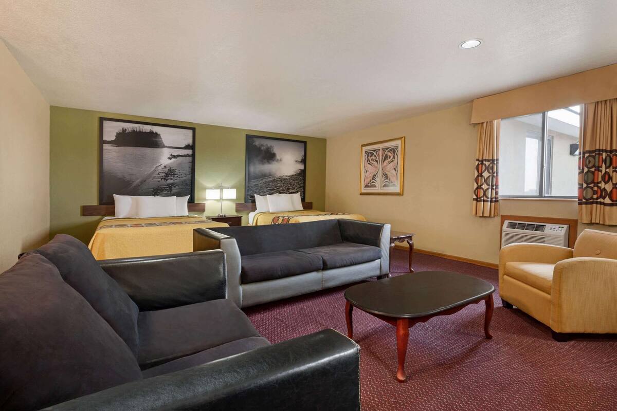 A hotel room with two beds, a sofa, a coffee table, and artwork on the walls.