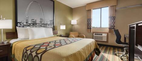 A hotel room with a large bed, a desk, a chair, a desk lamp, a window with curtains, and a wall-mounted air conditioning unit.
