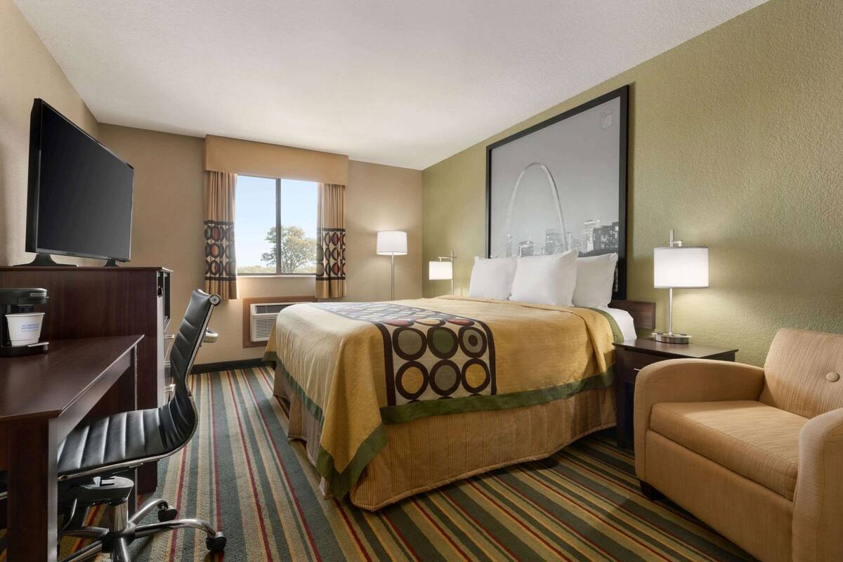 A hotel room with a bed, desk, chair, TV, and a cityscape view.
