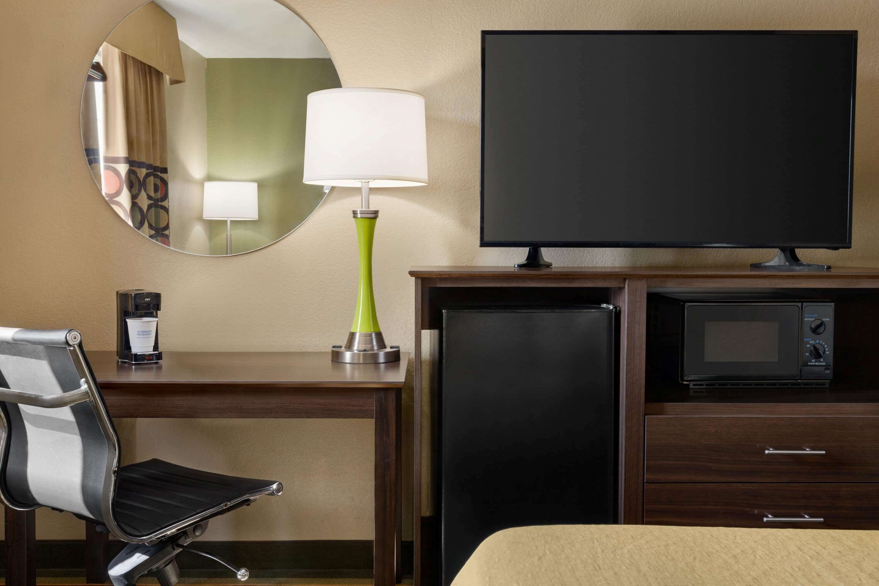 Habitación de hotel con cama, escritorio con lámpara, televisión, microondas y refrigerador.