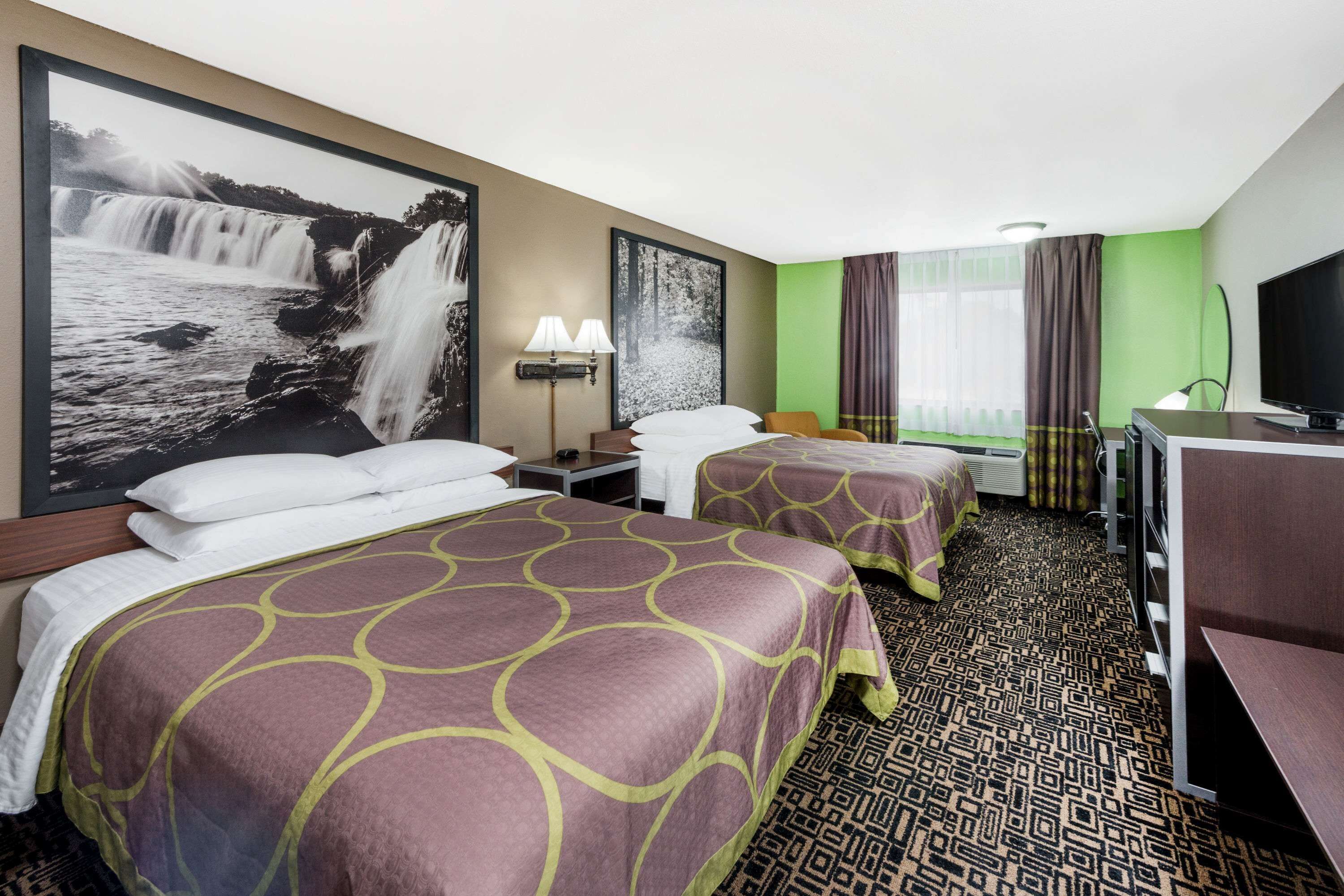 A hotel room with two beds, a desk, a TV, and a large waterfall painting on the wall.