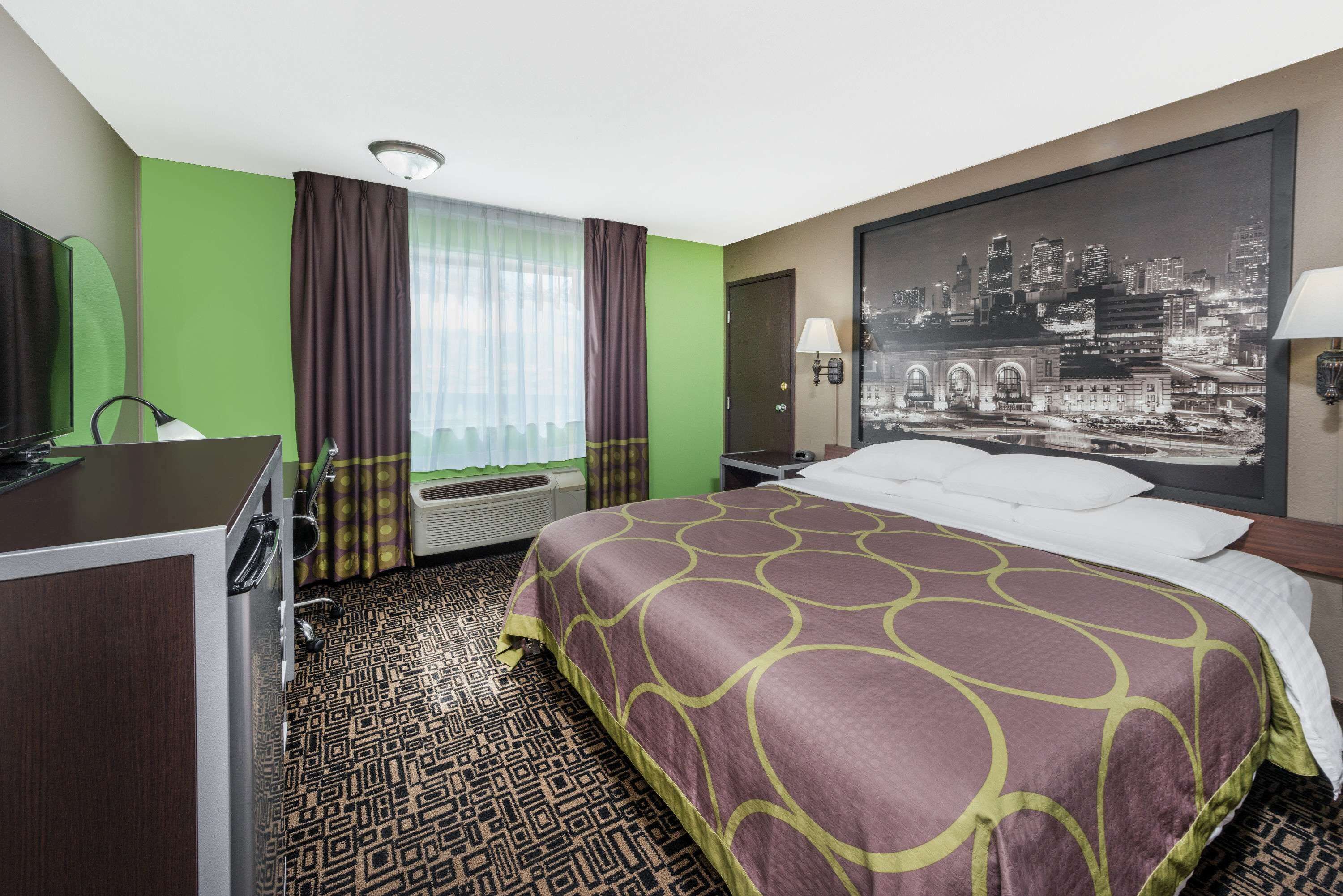 A hotel room with a bed, a desk, a television, and a cityscape painting on the wall.