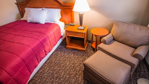 Une chambre d’hôtel avec un lit, une table de chevet avec une lampe, une chaise et une petite table.