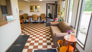 Un hall d’hôtel avec un sol à carreaux, un canapé, une petite table sur laquelle est posé un vase de fleurs et un comptoir de réception avec un téléphone.