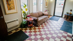 Une pièce avec un sol à carreaux, un canapé marron, une petite table sur laquelle est posé un vase de fleurs, et une porte qui donne sur l’extérieur.