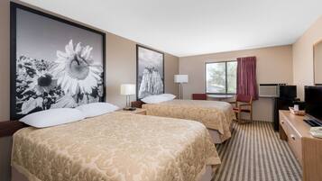 A hotel room with two beds, a desk, a TV, and large floral artwork on the walls.