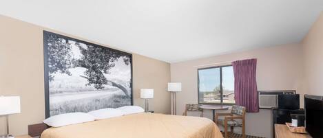 A hotel room with a large bed, a desk with a computer, a TV, and a window with curtains.