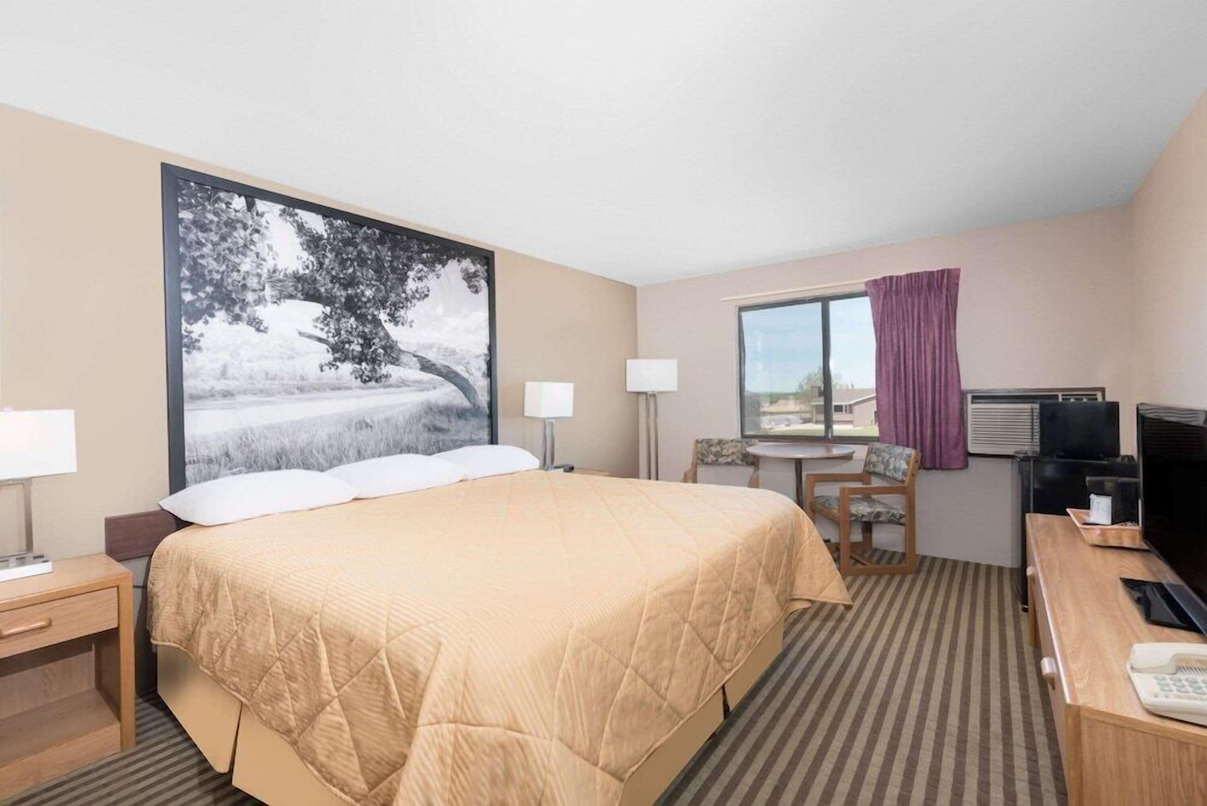 Habitación de hotel con cama, escritorio, silla, televisor y ventana con cortinas.