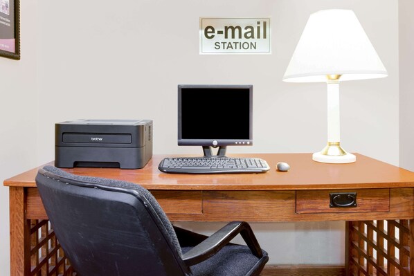 Un escritorio de madera con una impresora Brother, un monitor de computadora, un teclado, un ratón y una lámpara.