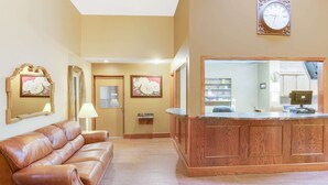 A spacious lobby with a leather sofa, wooden reception desk, and framed floral artwork on the walls.