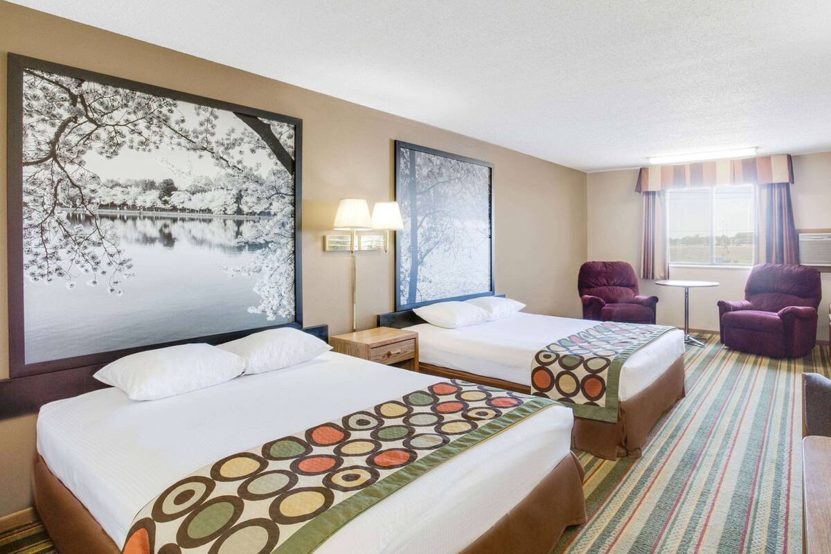 A hotel room with two beds, a large window, a chair, and a table.